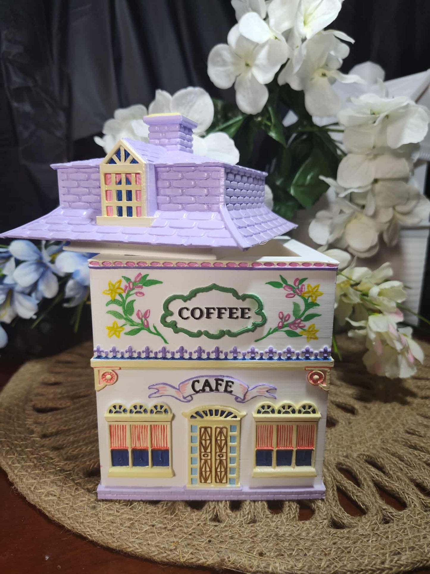 Decorative cookie jar shaped like a small building with 'Coffee Cafe' text, surrounded by white flowers.