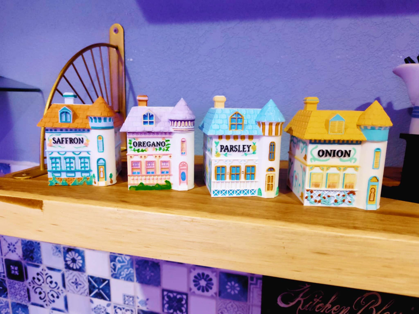 Four 3D printed, hand-painted spice jars shaped like miniature houses, labeled Saffron, Oregano, Parsley, and Onion, designed in a vintage Lenox-inspired style and displayed on a wooden shelf.