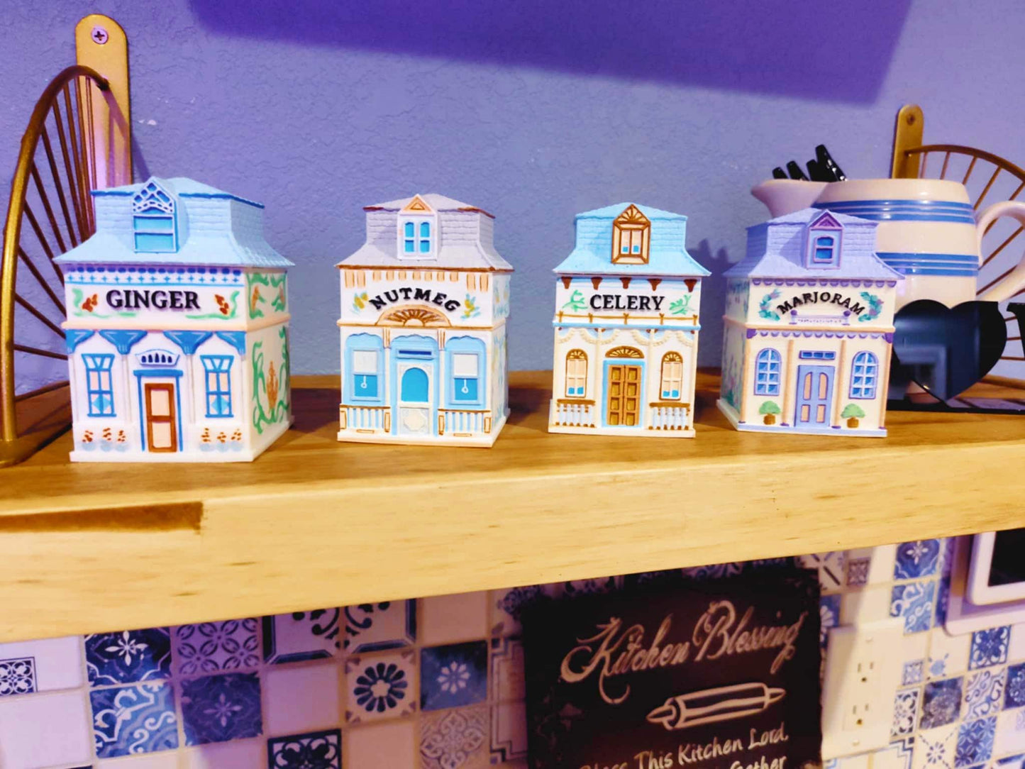 Four 3D printed, hand-painted spice jars shaped like miniature houses, labeled Ginger, Nutmeg, Celery, and Marjoram, inspired by vintage Lenox village designs and displayed on a wooden shelf.