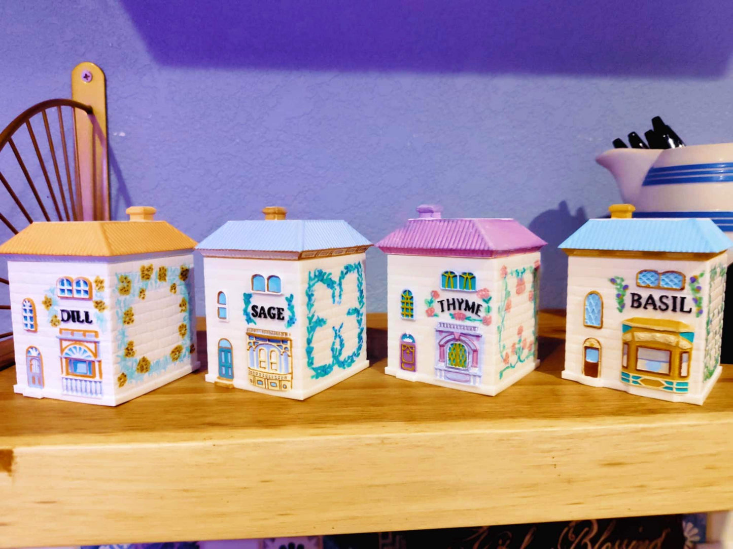 "Four 3D printed, hand-painted spice jars shaped like small houses, labeled Dill, Sage, Thyme, and Basil, designed in a vintage Lenox-inspired style and displayed on a wooden shelf.