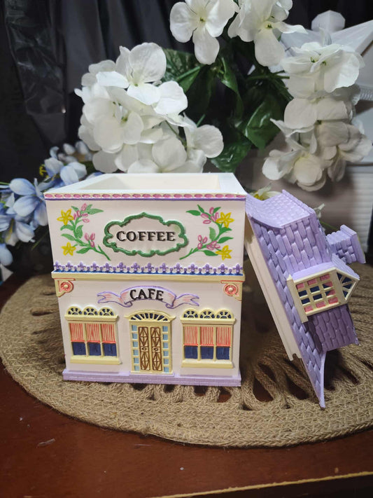 Decorative model of a coffee shop with a small purple building on a textured surface.