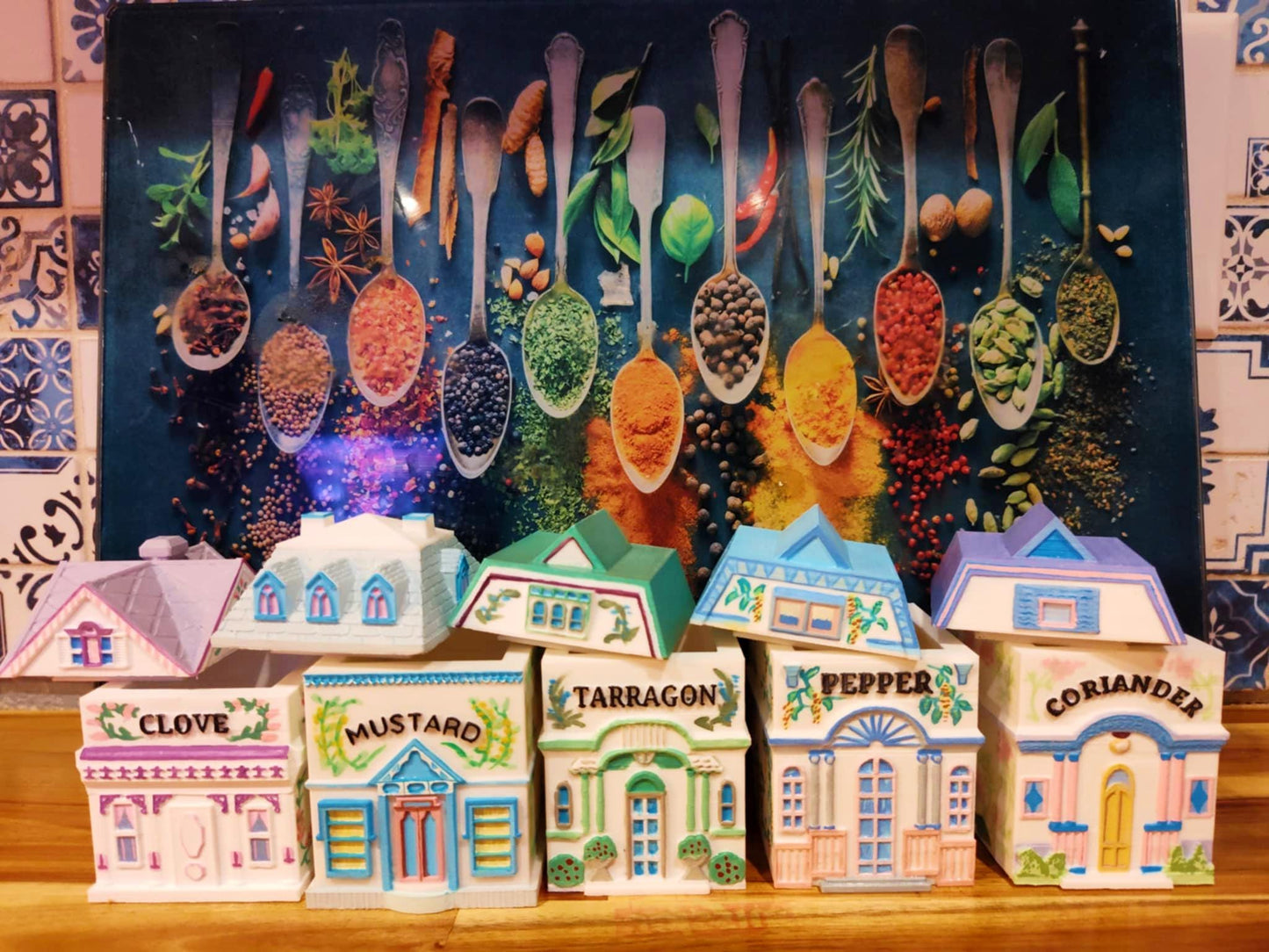 Set of five open 3D printed, hand-painted house-shaped spice jars labeled Clove, Mustard, Tarragon, Pepper, and Coriander, inspired by Lenox designs, displayed in front of a colorful spice-themed backdrop.