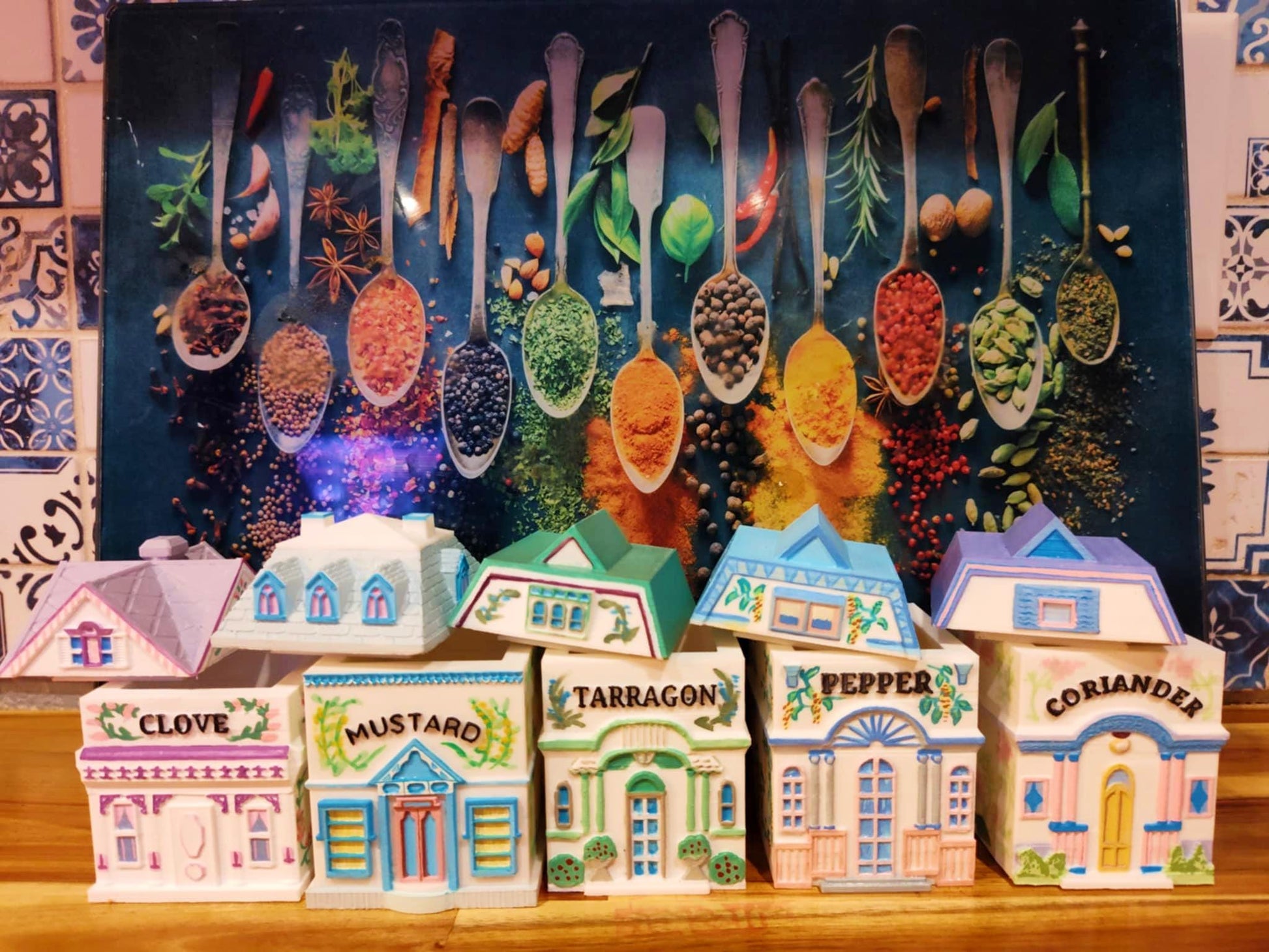 Set of five open 3D printed, hand-painted house-shaped spice jars labeled Clove, Mustard, Tarragon, Pepper, and Coriander, inspired by Lenox designs, displayed in front of a colorful spice-themed backdrop.